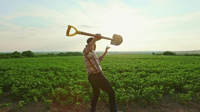 Back view of farmer wearing plaid shirt, dancing on field, growing plants. Young man working in countryside, growing sprouts. Concept of growing and taking care of plants.