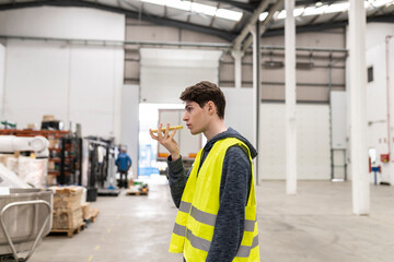 Young Caucasian worker sending a voice message to get the job done in a factory