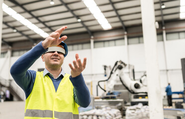 Caucasian worker in safety helmet and reflective vest working with virtual reality goggles in a robotic factory.