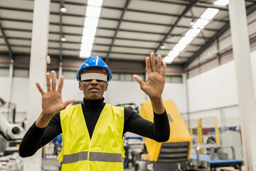 African-american worker with safety helmet and reflective vest working with virtual reality glasses in a robotic factory warehouse.