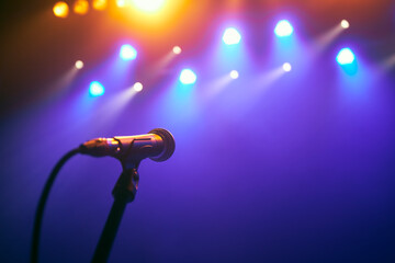 Selective focus on lluminated microphone on stage against colorful spotlights...