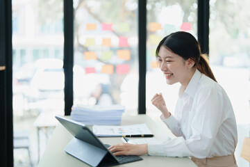 Portrait of a woman business owner showing a happy smiling face as he has successfully invested her business using computers and financial budget documents at work