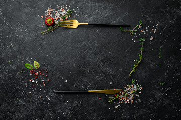 Cutlery on a black stone table with vegetables and spices. Food background. Top view. Rustic style.