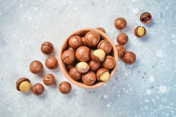 Obraz premium Macadamia nut. Macadamia nuts in a shell, in a bowl. On a stone background. Macadamia nuts are rich in various trace elements and vitamins.