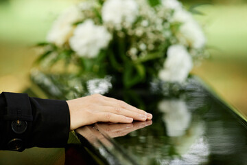 Close up of female hand on coffin saying goodbye at outdoor funeral ceremony, copy space - obrazy, fototapety, plakaty