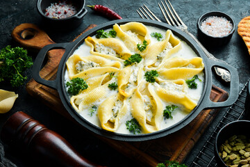 Traditional Italian lunch. Shell-shaped pasta with meat, cream sauce and parmesan. In a frying pan. On a stone background. Recipe.