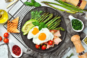 Breakfast. Scrambled eggs, asparagus, bacon and avocado. On a black stone plate.