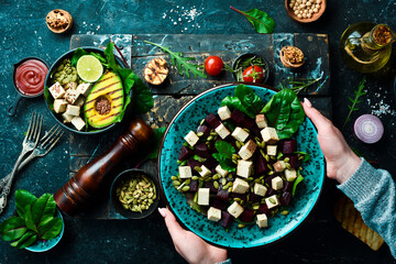Female hands holding a bowl of beet salad, tofu cheese, spinach and pumpkin seeds. The concept of healthy eating. Top view.