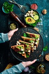Sandwich for Breakfast. Belgian waffles with avocado pate, sun-dried tomatoes and tofu cheese. The concept of dietary nutrition. On a stone background.