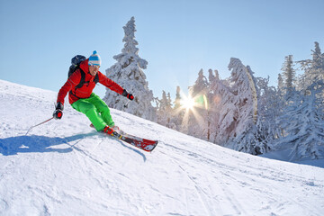 Skier skiing downhill in high mountains against against the fairytale winter forest with sunset.