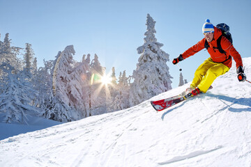 Skier skiing downhill in high mountains against against the fairytale winter forest with sunset.