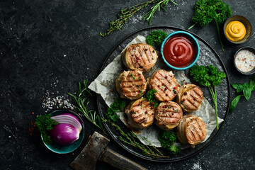 Grilled medallions wrapped in bacon. in a pan, ready to eat. On a black concrete background. Top view.