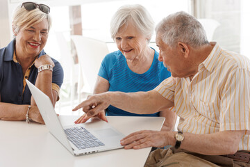 gruppo di tre anziani  seduti comodamente intorno a  un tavolino osservano lo schermo di un...