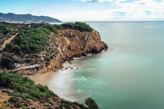 Nice cliff in the mediterranean sea near Sitges and Vilanova i la Geltru, spain. Long exposure photography on a sunny day overlooking the dead man's beach, horizontal.