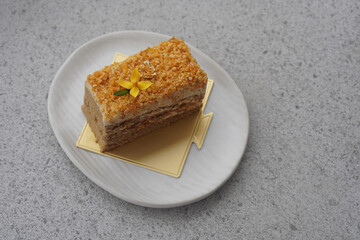 one yellow flower and green leaf on coffee almond crunchy cake on gold paper on white ceramic plate, on grey marble background, dessert, food, snack, copy space