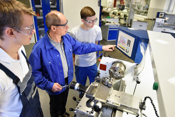 young apprentices in technical vocational training are taught by older trainers on a cnc lathes machine - 549971822