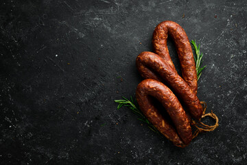 Smoked homemade sausage ring. Sausage on a black stone background. Top view. - obrazy, fototapety, plakaty