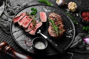 Grilled ribeye beef steak. Steak on a fork on a black plate. Top view. On a black stone background.