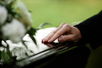 Closeup of womans hand on coffin saying goodbye at outdoor funeral ceremony, copy space - obrazy, fototapety, plakaty