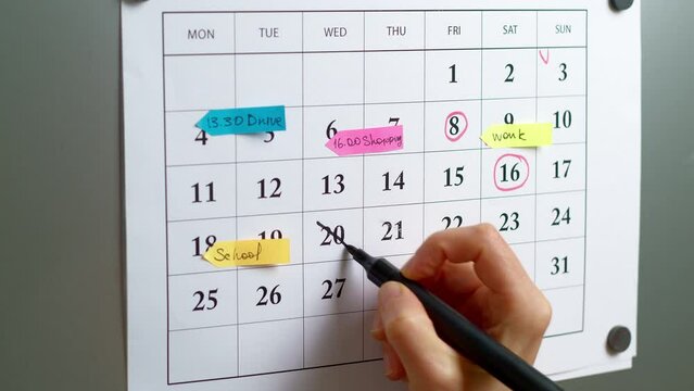 A woman marks the day on the calendar by planning a month for meetings and events.