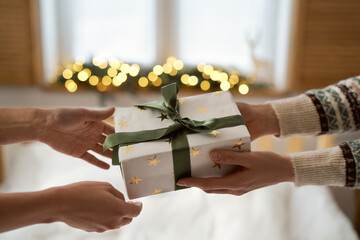 Hands of two unrecognizable people sharing Christmas present in bedroom