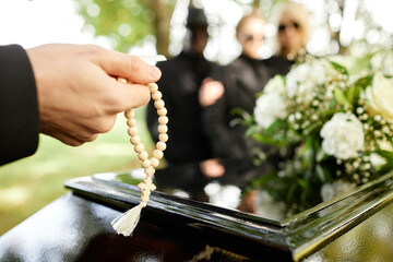 Close up of man holding rosary and praying at outdoor funeral ceremony, copy space