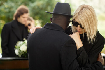 Two people embracing at outdoor funeral ceremony and wearing black