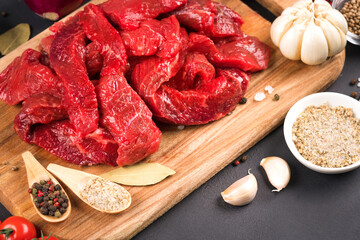 Chopped raw beef or lamb meat with seasoning, herbs and vegetables on wooden cutting board. Organic veal meat for cooking stew, azu or other meat main dish