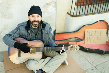 Smiling homeless man singing a song with a guitar on the street