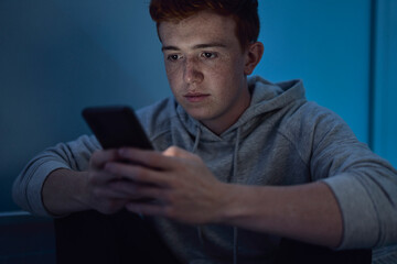 Focus caucasian teenage boy using mobile phone while sitting at night in his room