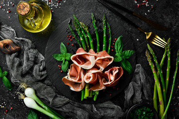 Grilled asparagus with prosciutto and basil. On a black stone background. Top view.