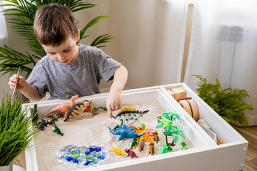 Cute baby boy playing sensory box kinetic sand table with carnivorous and herbivorous dinosaurs