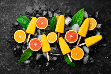 Citrus frozen popsicles on ice. Cold summer fruit sweets. On a stone background.
