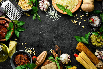 Cooking background: pasta, basil, parmesan, pesto, tomatoes and nuts, olive oil. On a black stone background background.