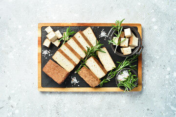 Fresh tofu cheese. Smoked tofu cheese with spices cut into pieces on a board. Vegan healthy food. On a stone background.