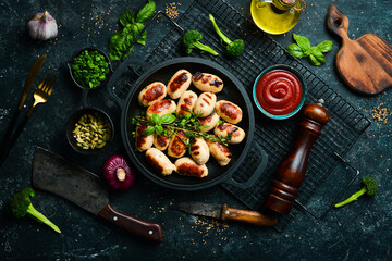 Mini grilled sausages on a frying pan. Barbecue. Meat menu. Top view. On a stone background.
