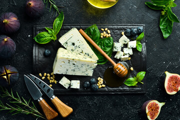 Blue cheese with mold on a black stone plate with basil and honey. On a black stone background. Top view.