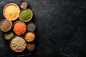 Legumes, a set consisting of different types of beans, lentils and peas, rice and buckwheat on a black background, top view. The concept of healthy and nutritious food