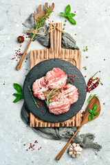 Raw cutlets in bacon served on a black plate with rosemary and thyme. On a gray background. Top view.