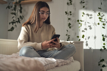 Caucasian teenage girl browsing phone while sitting on bed