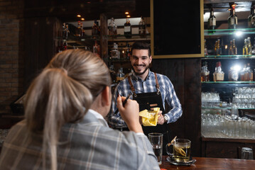 Young lonely business woman sitting at the bar wooden counter working and talking with the bartender. Customer chatting with employee at the cafeteria.