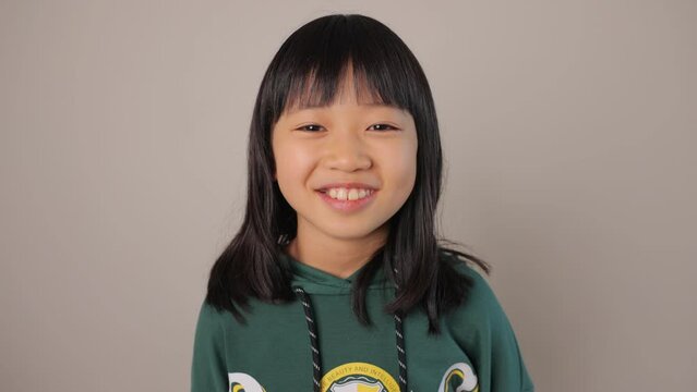Little asian teen girl smiles at the camera. Dolly in.