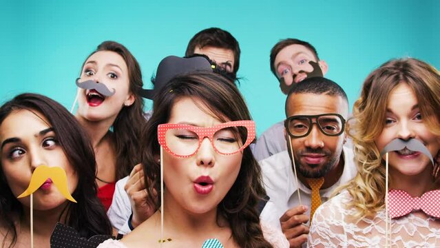 Group of friends, dance and party props in studio on blue background. Diversity, face mask and people in comic, funny or crazy facial disguise celebrating holiday and dancing at social event together