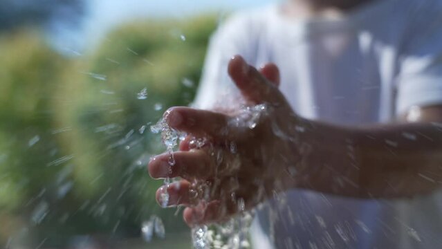 Child washing hands at water fountain outdoors. Little boy cleaning hand close up splashing water in slow motion