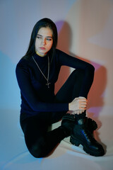 The girl is a model with dark hair, in a blue jacket, black trousers and thick-soled shoes. Portrait of a young woman on a white background.
