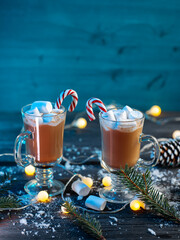 Hot cocoa with marshmallows and cinnamon on a blue wooden table. Christmas tree branches, candy cane and round garland