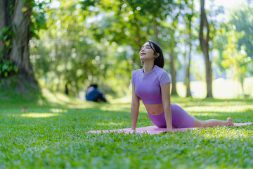 Naklejka na ściany i meble Fitness woman doing yoga in park, calm and relaxing women's happiness blurry background Asian woman meditating while practicing yoga concept of freedom peace and relaxation healthy