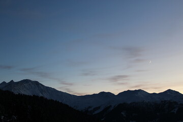 Sunset over Swiss alpine mountains. Silhouette of a mountain range against sky at sunset with gradient from indigo to light pale yellow. Snow on peaks