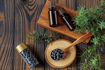Fresh purple organic juniper berries in a wooden spoon and a bottle of oil on a wooden background top view