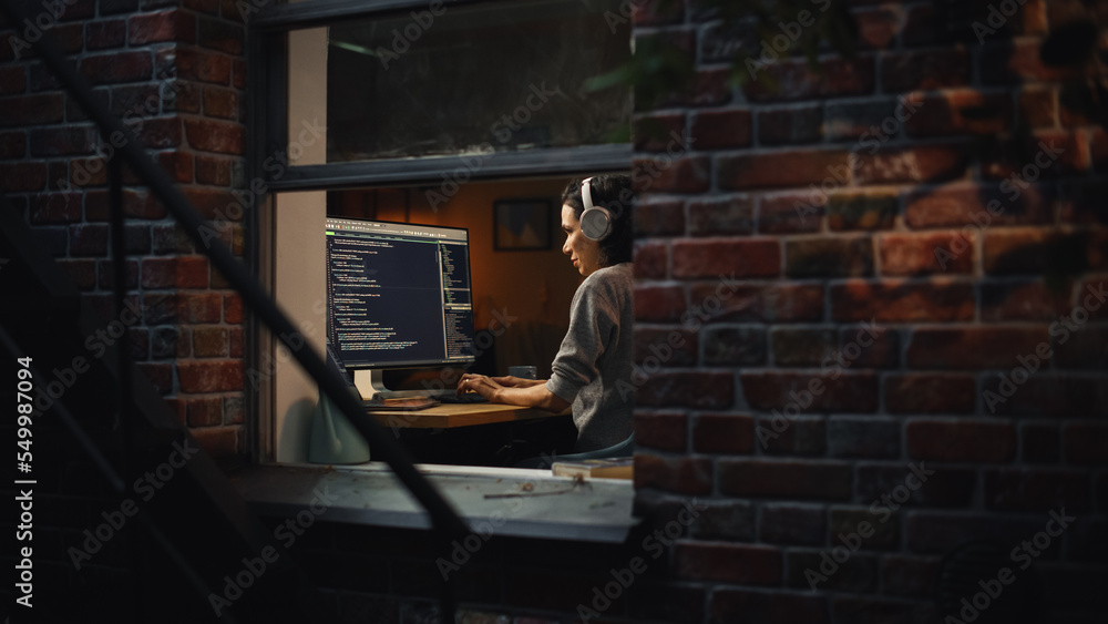 Poster Latin Female Digital Startup Entrepreneur Working on Computer Late at Night. Software Developer Working on Innovative e-Commerce App. Overworking Concept. Shot Into the Window From Outside.